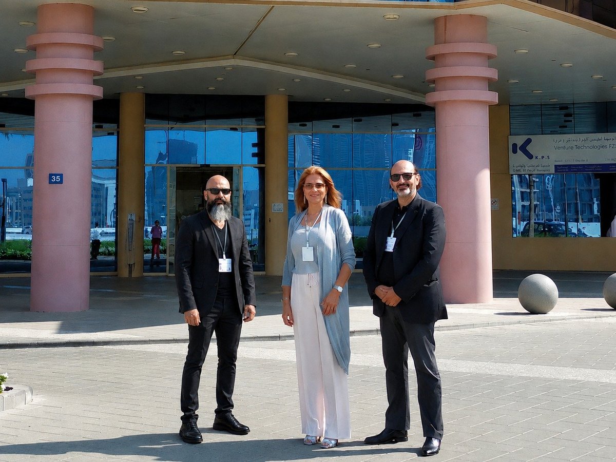 Three people in business attire posing in front of a modern building with pink columns and large windows