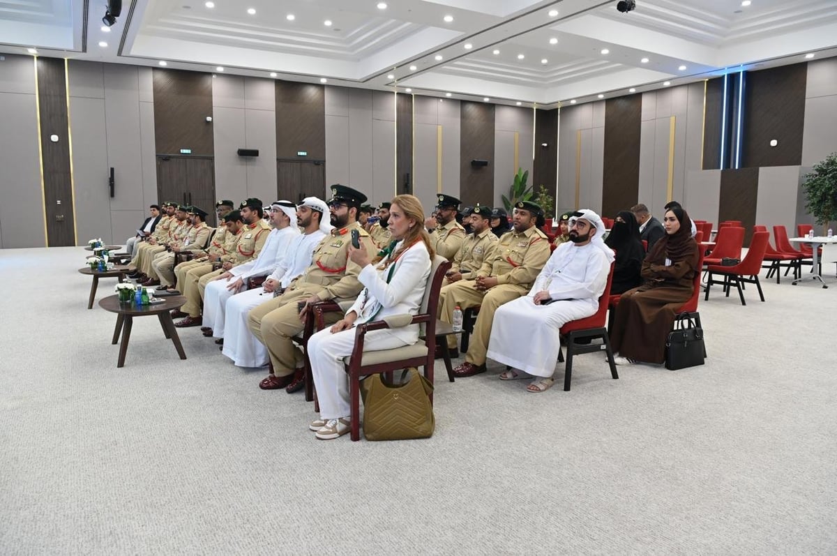 A diverse group of people seated in a semi-circle during a formal meeting or conference in a modern white banquet hall.