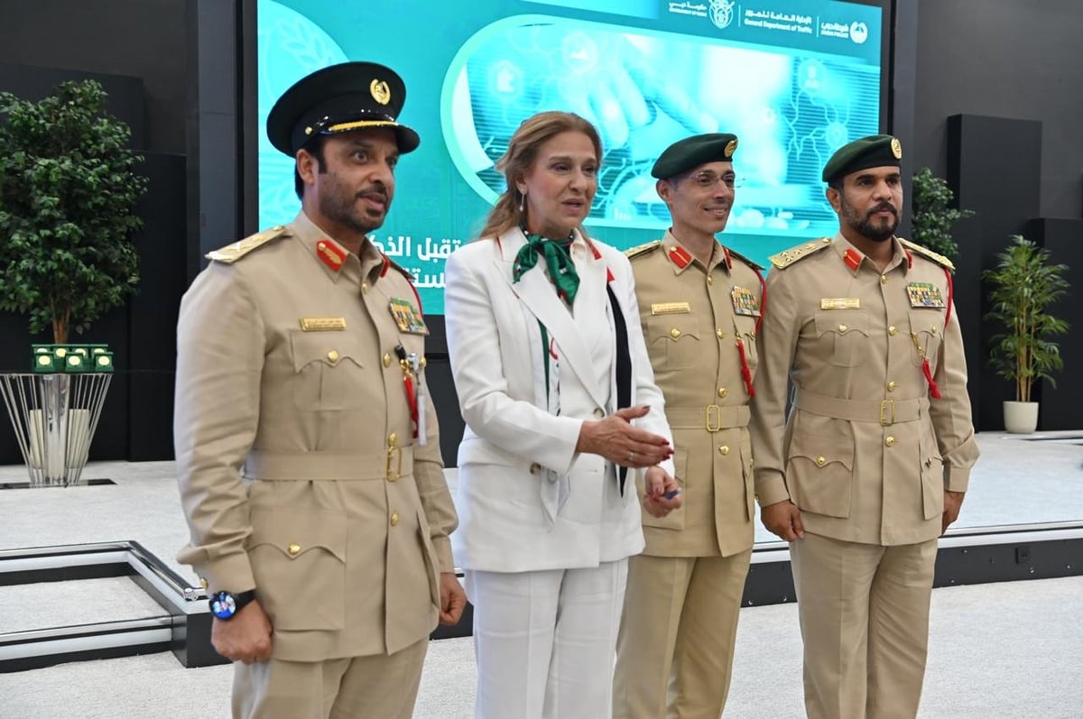 Four military officers and officials stand in front of a large display screen at an indoor event venue.